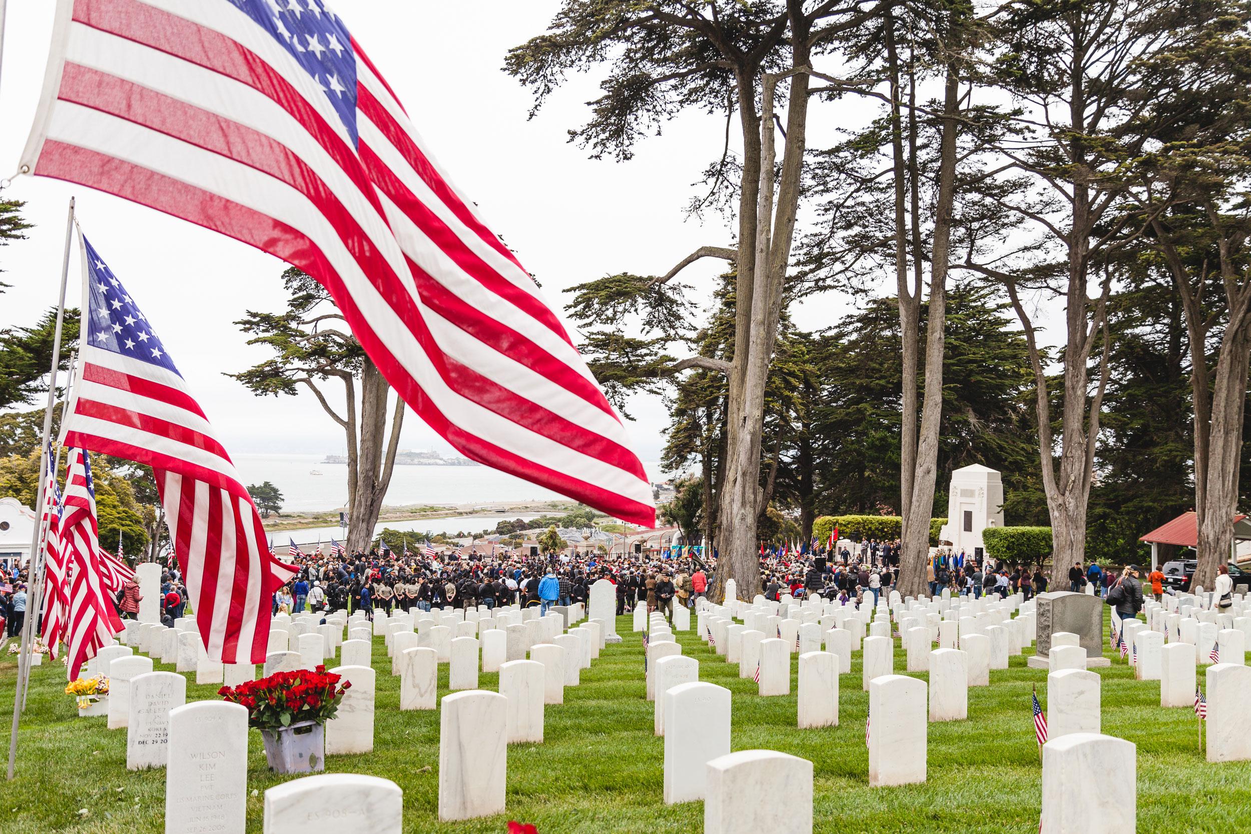 US flags and grave sites with Memorial Day visitors in background.